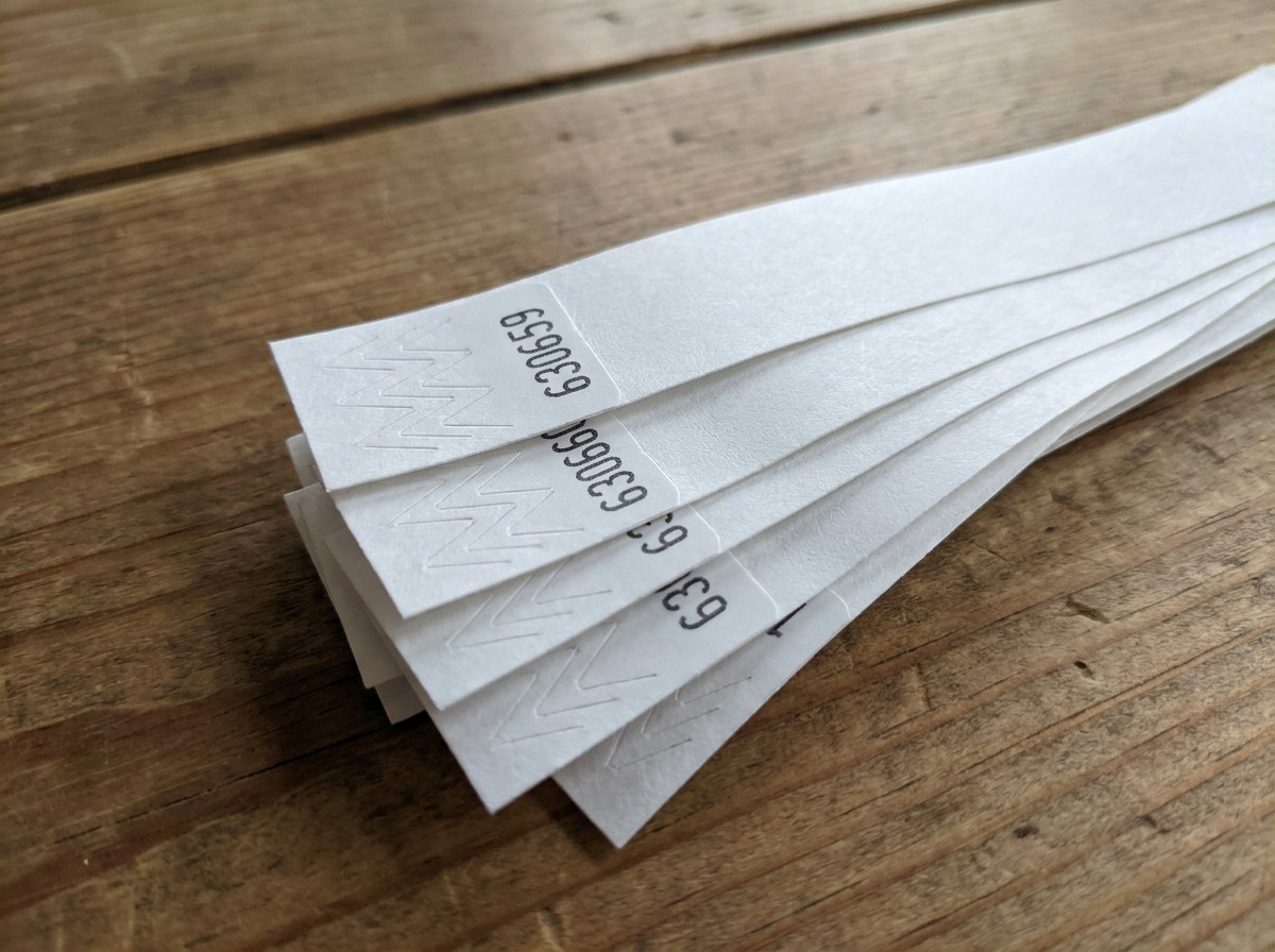 Nahaufnahme von Tyvek-Armbändern mit aufgedruckter sequenzieller Nummerierung in Schwarz, fächerförmig auf einem Zugangskontrolltisch bei einer Veranstaltung angeordnet